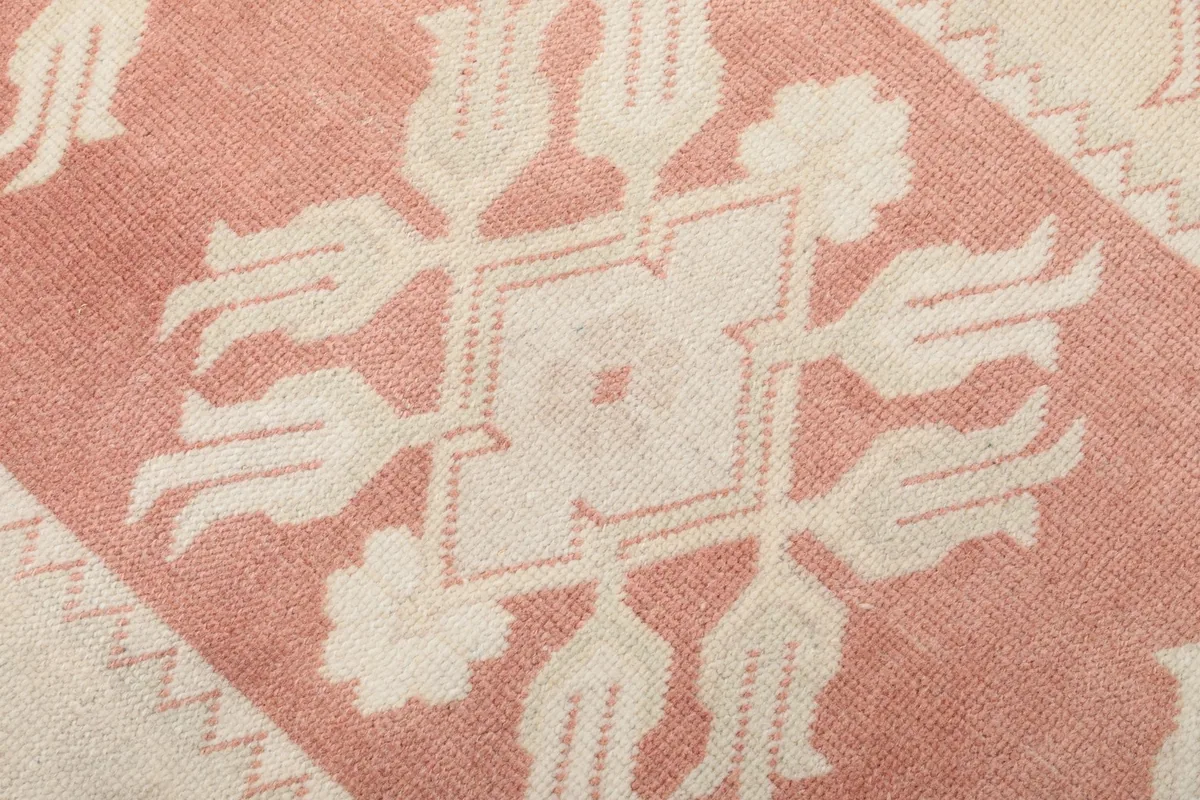 Macro detail of a single ivory floral motif against the rose background, showing wool pile texture.