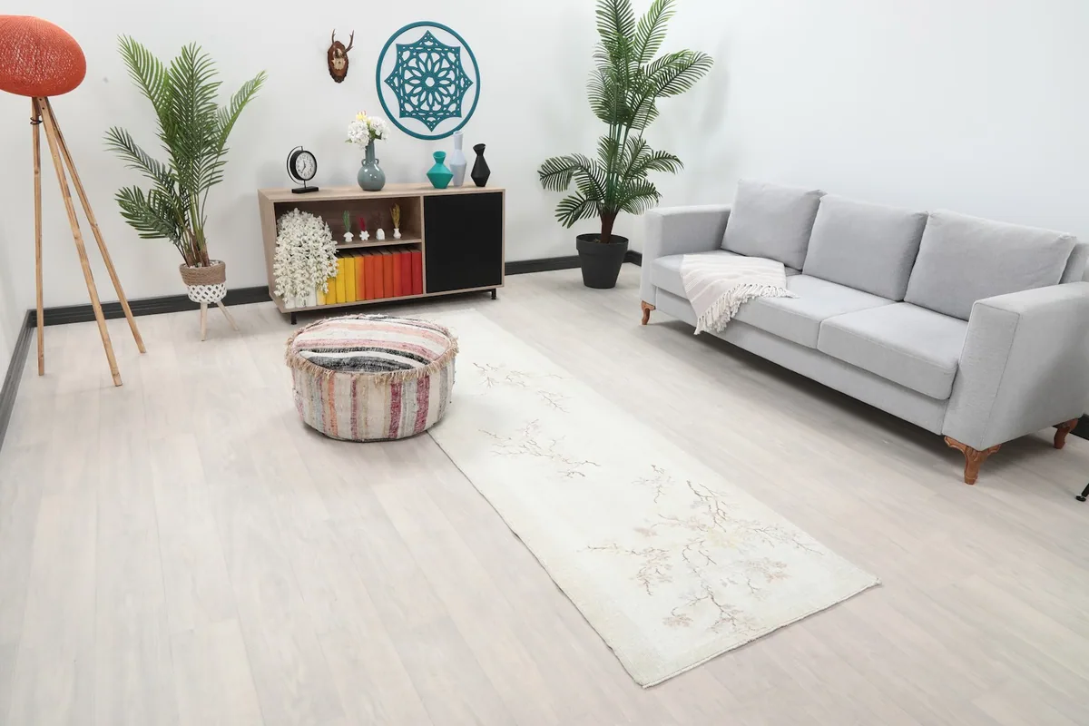 An ivory Anatolian runner rug with subtle floral patterns extending from a gray sofa towards a colorful ottoman.