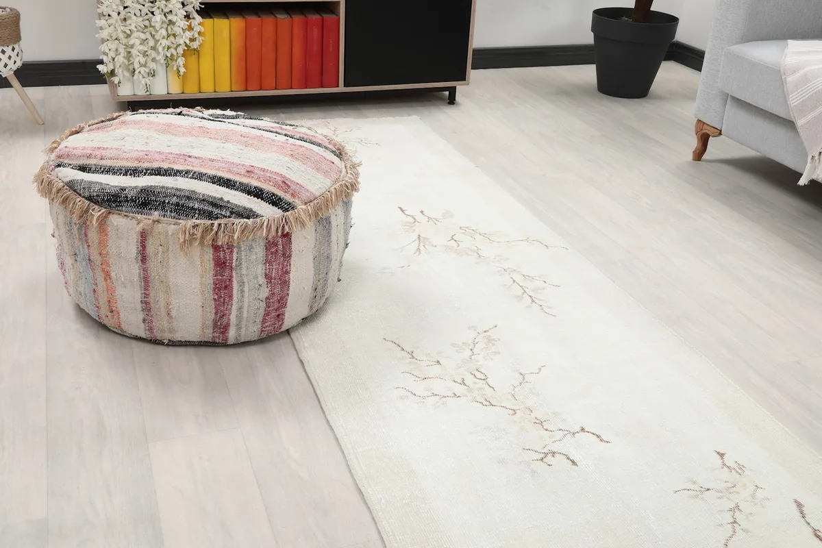 Close-up view of the ivory runner rug's branch motif next to a striped ottoman, highlighting color and texture.