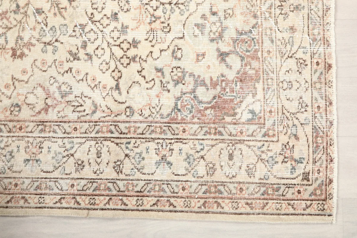 Detailed view of the rug's border design featuring intricate floral and geometric elements in faded colors