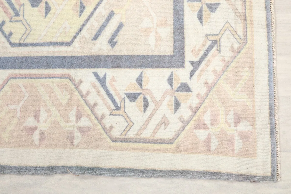 Detail of the rug's corner, showing geometric patterns in beige, tan, and blue hues.