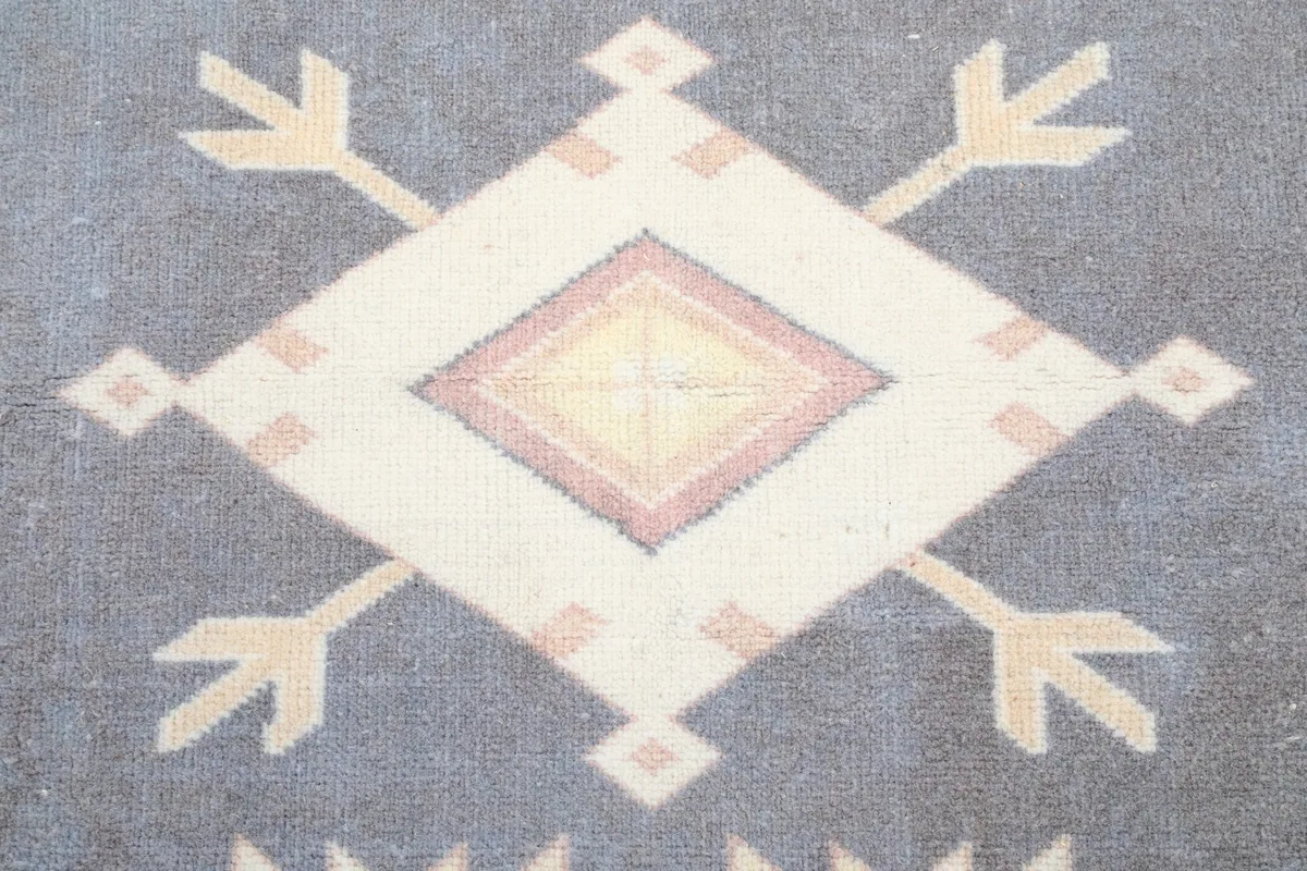 Close-up of a large central diamond motif in yellow, beige, and red on the blue field of the rug.