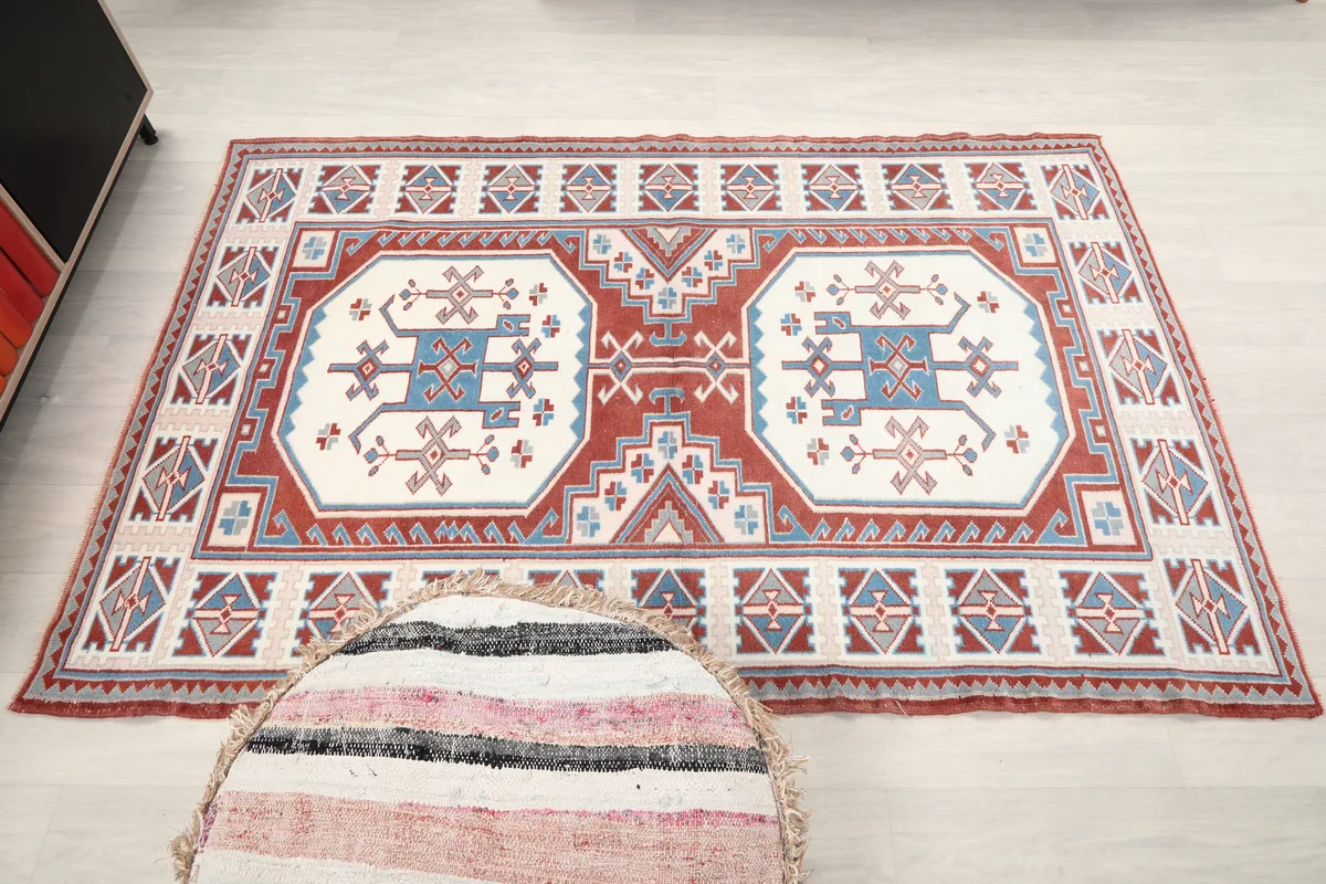 Overhead view of the Rust Ivory Geometric Anatolian Rug in a room, next to a striped pouf