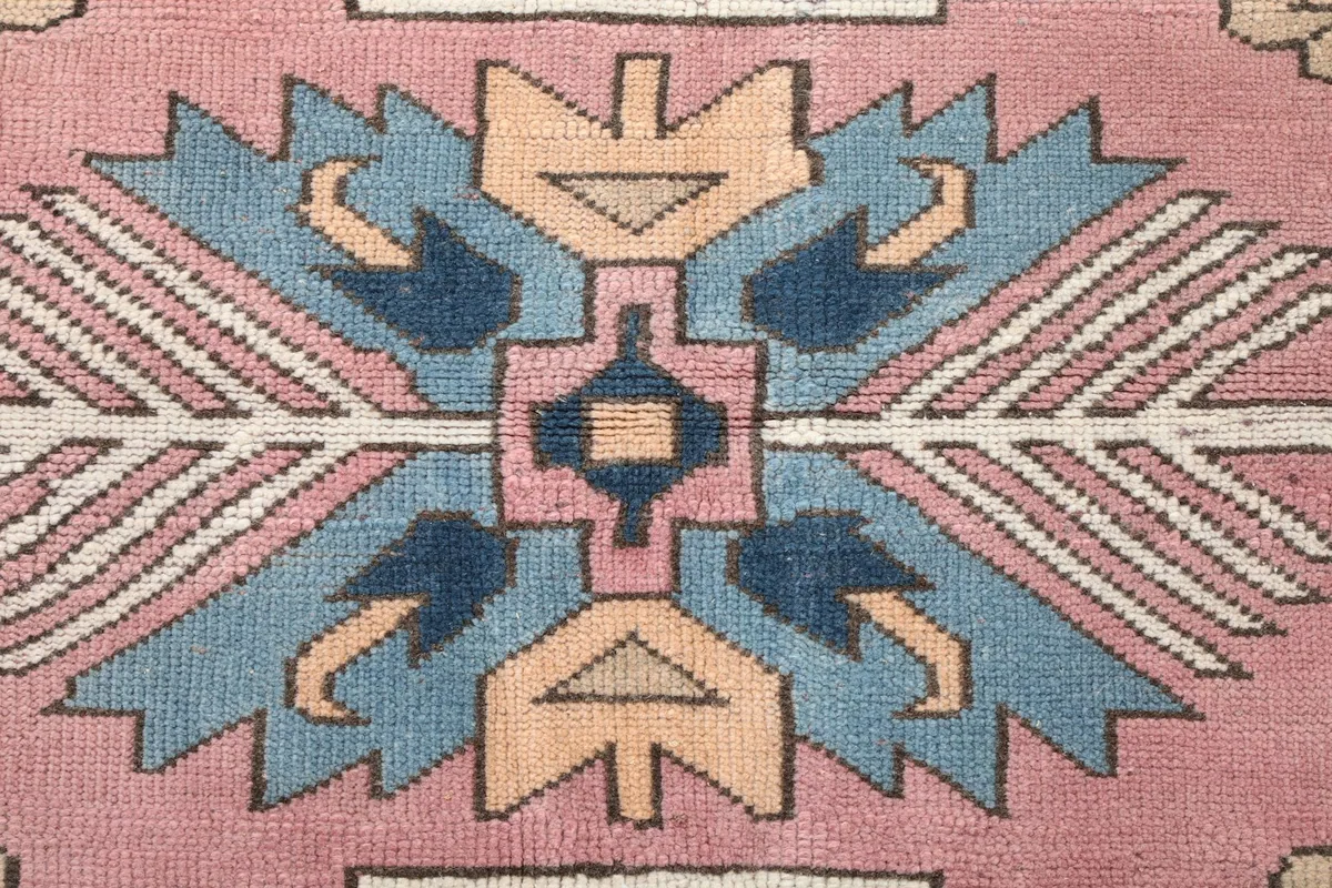 Intricate detail of a central tribal motif in blue, rose, and tan, showcasing the hand-knotted craftsmanship.