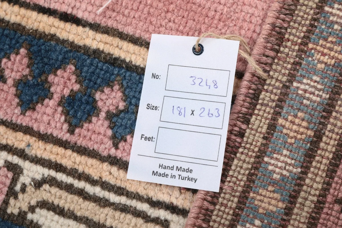 Close-up of the product tag indicating the rug's dimensions of 181 x 263 cm and handmade origin.