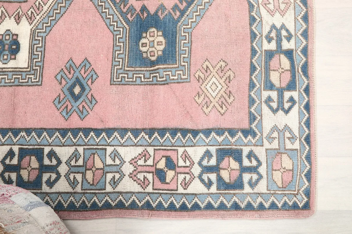Detail of the rug's outer border with blue, ivory, and rose tribal patterns