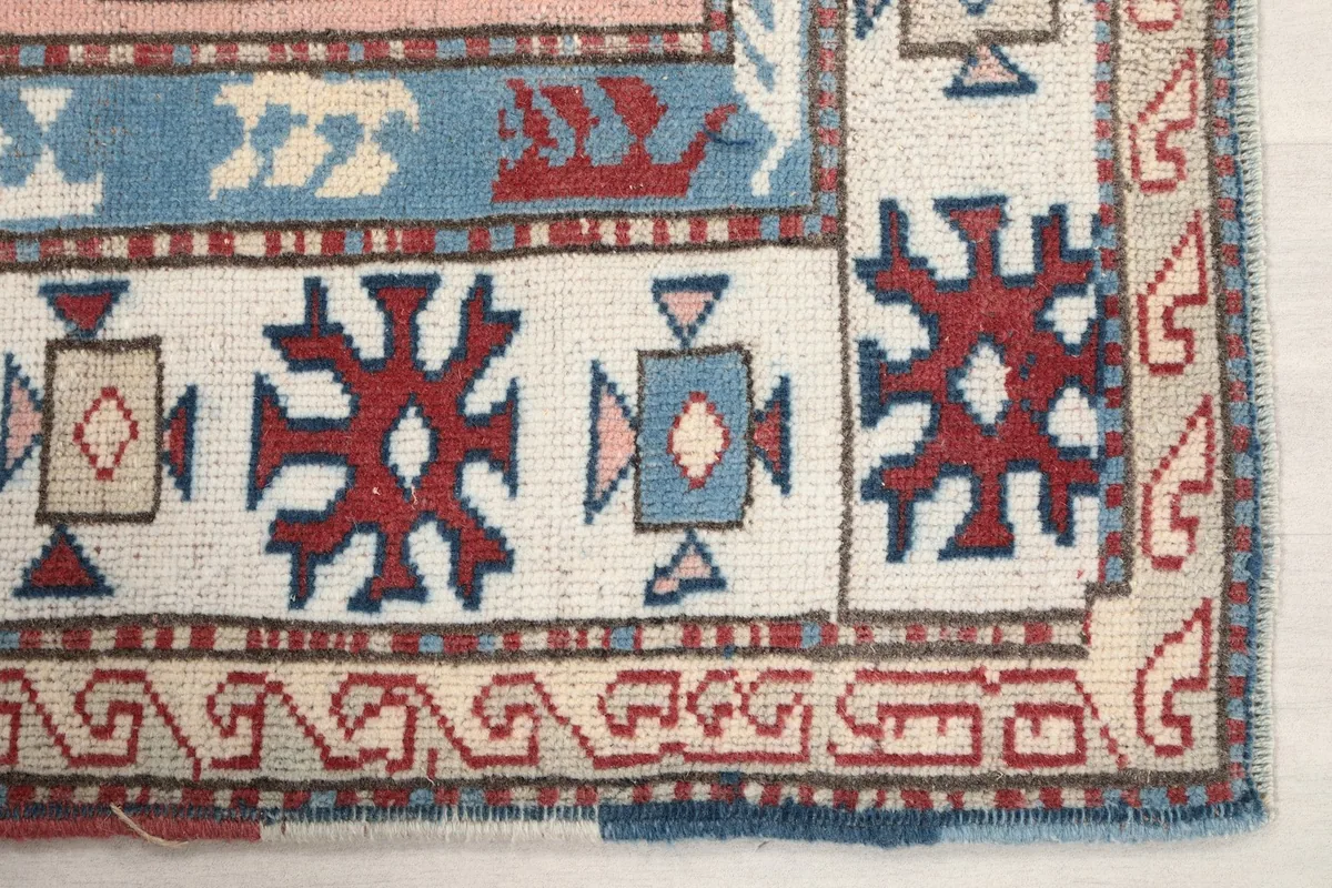 Detail of the ivory border with red and blue tribal patterns in the corner of the rug