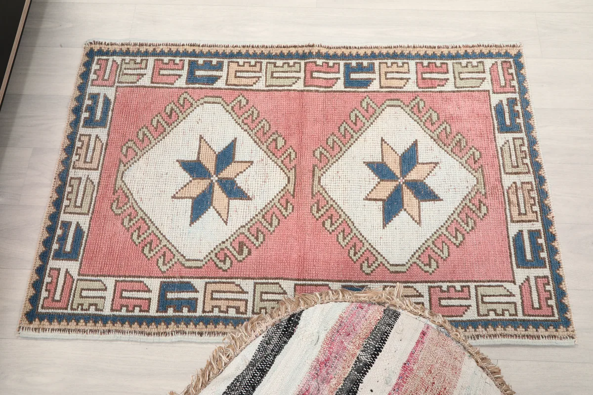 Rose Geometric Star Rug, full view in a room, with an ottoman partially obscuring the foreground.