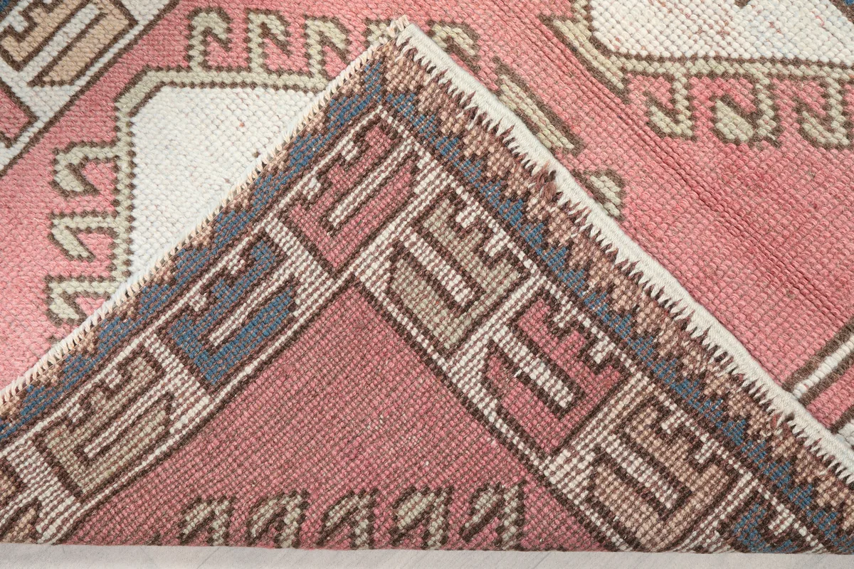 Rose Geometric Star Rug, corner folded back to reveal the cotton foundation and hand-knotted construction.