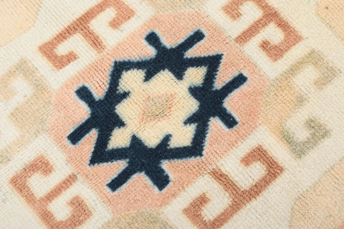 Macro detail of the hand-knotted wool pile, highlighting a navy star motif within a pinkish-rust pattern