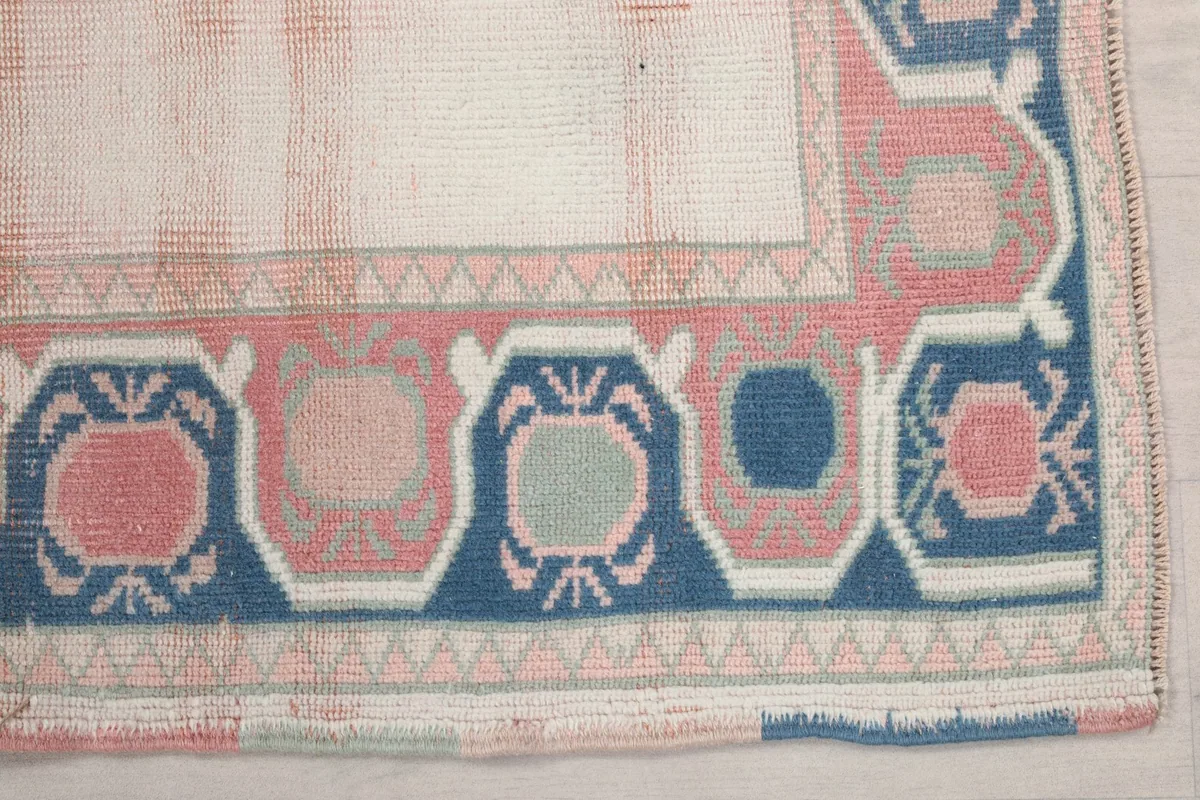 Detail of the rug's border showing navy, rose, and gray geometric motifs and fringe