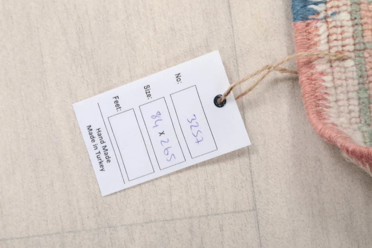 Care label attached to the rug, indicating hand-made in Turkey and size in centimeters