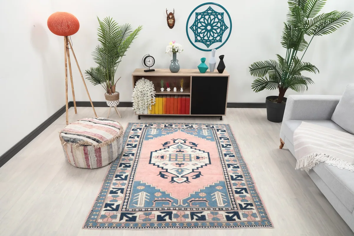 Vintage pink and blue Anatolian rug displayed in a living room setting with a sofa and plants