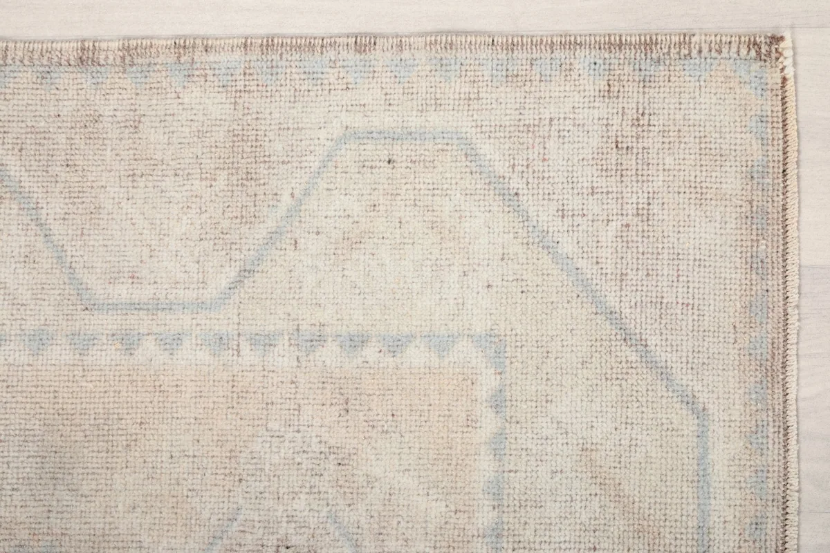 Detailed view of the upper left corner of the beige rug, highlighting the blue geometric border design
