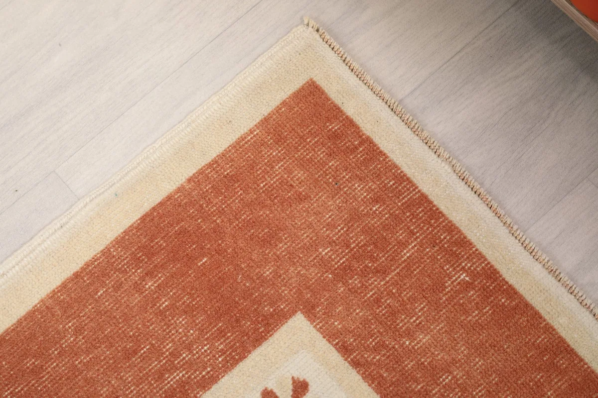Corner detail of the rug, showing the transition from the rust border to the ivory field and the edge