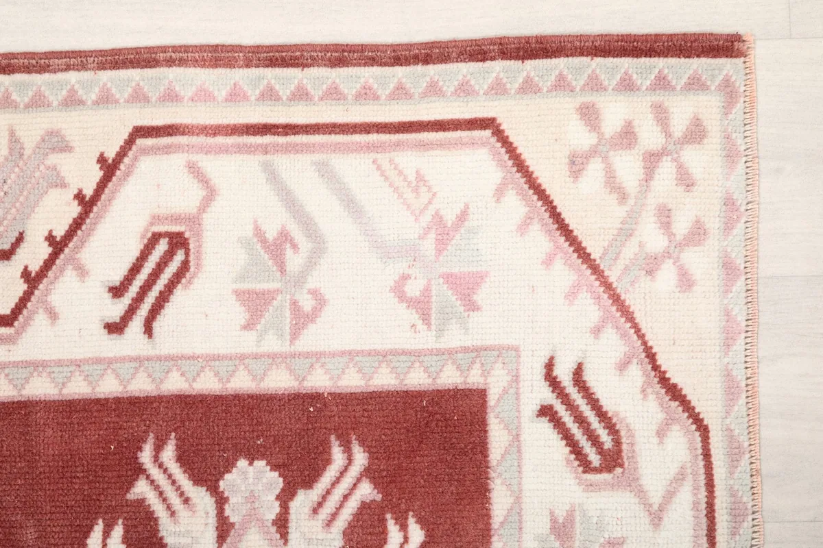 Detail of the rug's corner, highlighting the ivory border with pink and gray tribal patterns