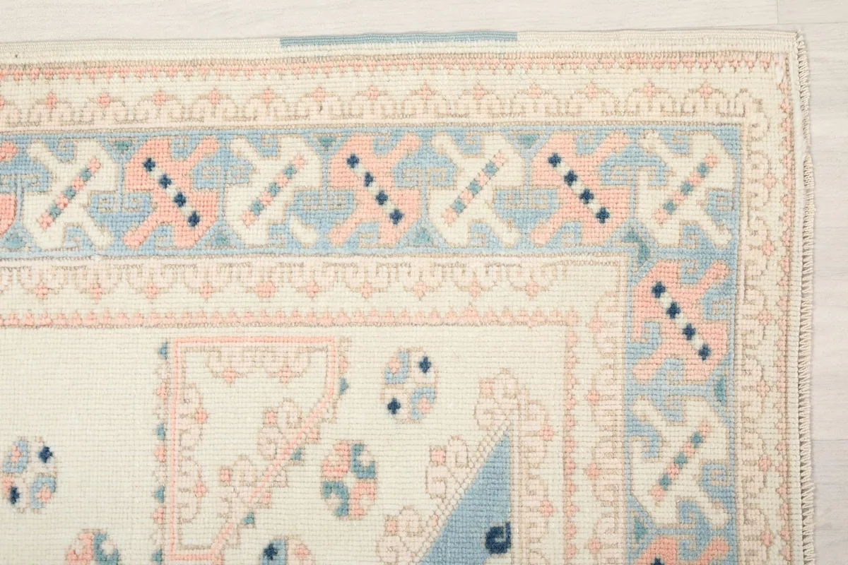 Detailed view of the rug's corner border, displaying intricate geometric motifs in rose, blue, and ivory.