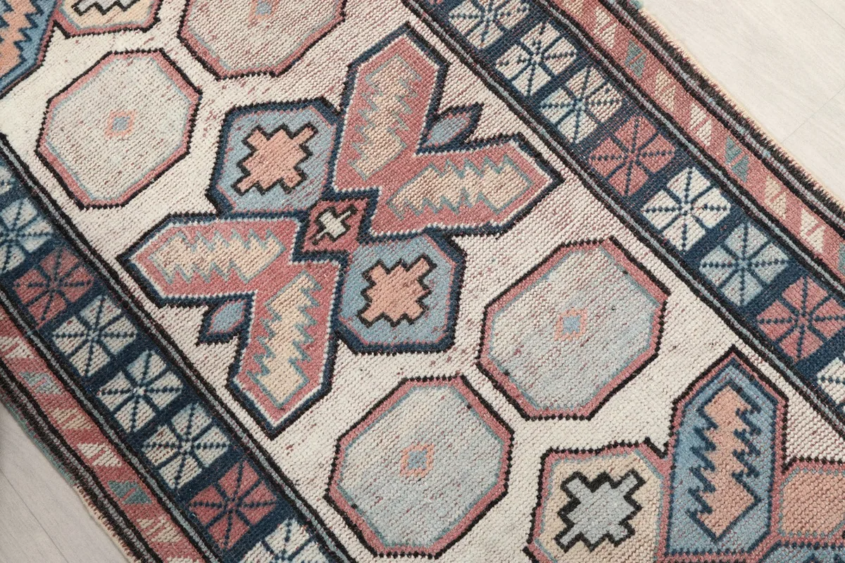 Diagonal view highlighting the central geometric motifs in rose, navy, and blue on the cream field.