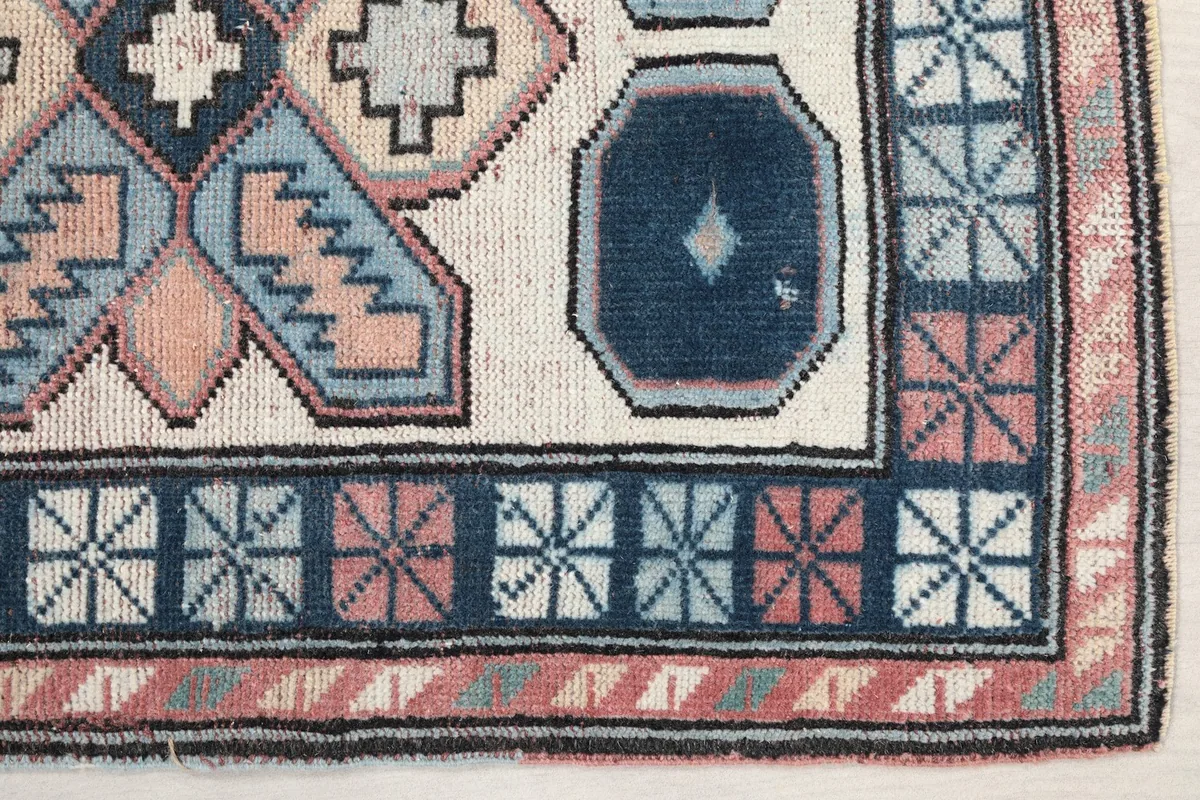 Detailed view of the navy and rose geometric border pattern and corner of the hand-knotted rug.
