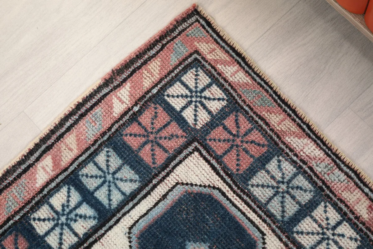 Close-up of a rug corner, revealing the outer rose border and inner navy geometric border details.