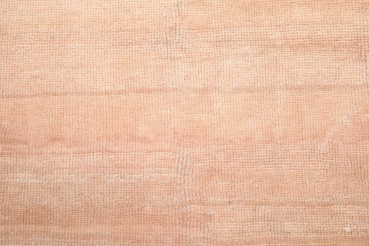 Close-up texture of the low wool pile in the orange central field of the rug