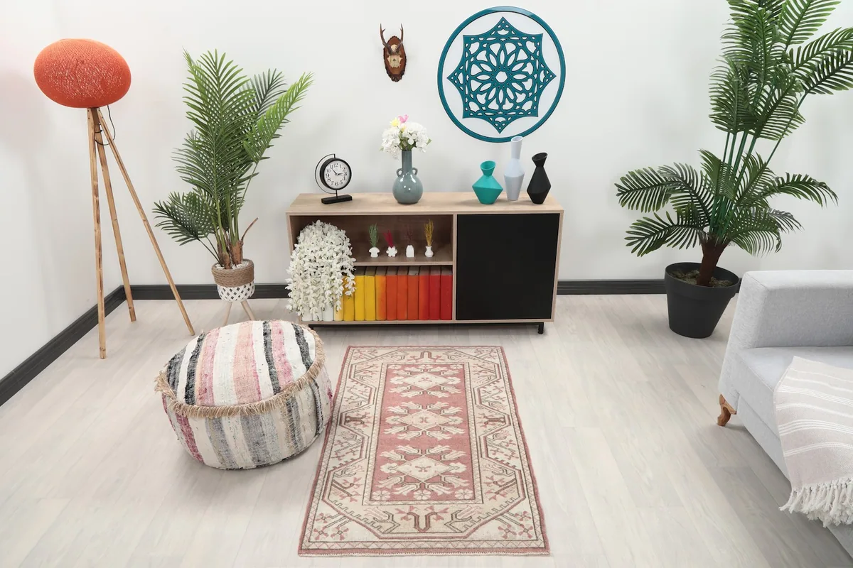 Rose and ivory vintage rug placed in a modern living space with a striped pouf and wooden furniture