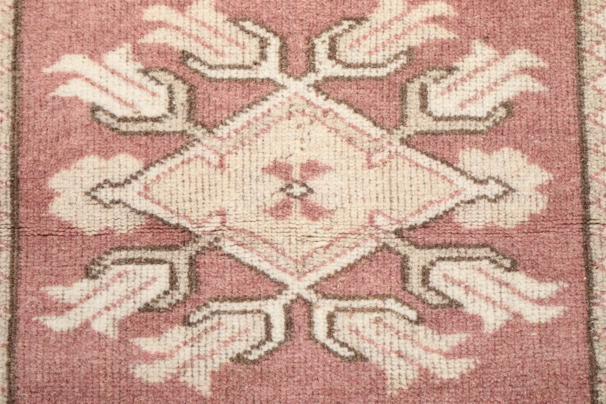 Close-up of a central geometric medallion with stylized floral elements in rose and ivory
