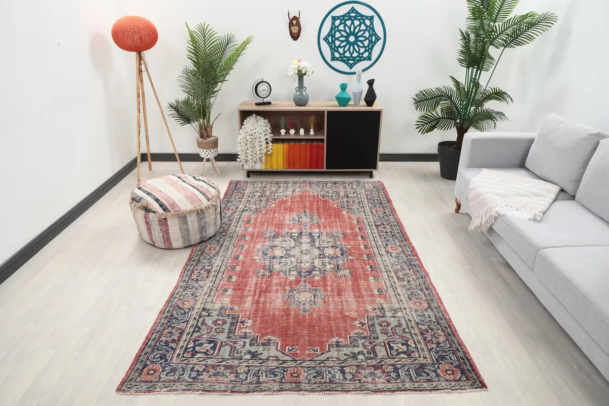 Vintage red and navy Anatolian rug in a living room setting with a sofa and pouf
