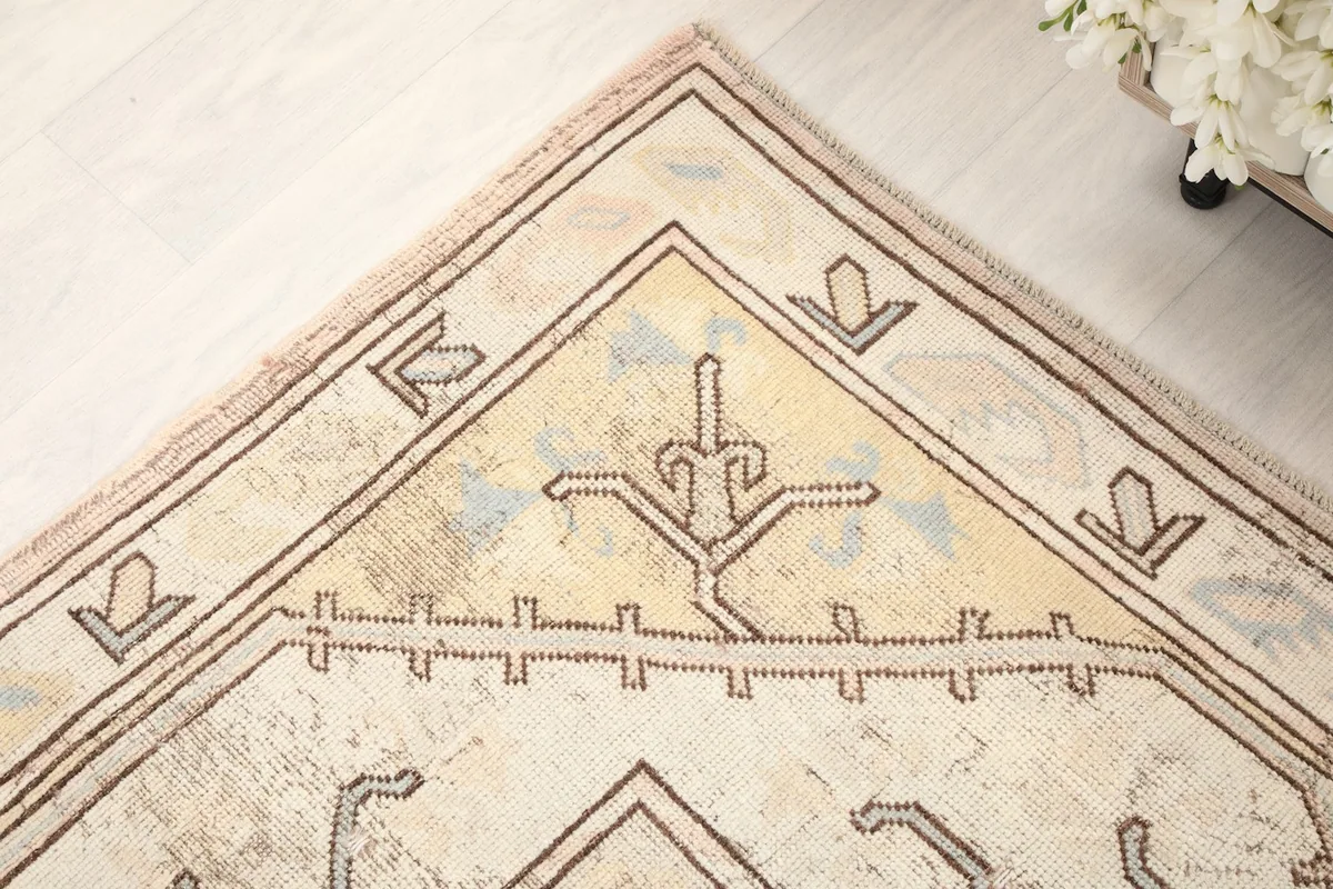 Close-up of a corner of the rug, revealing the faded rose and tan elements within the geometric border.