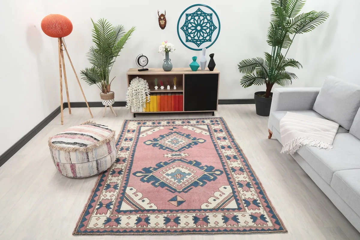 Rose and navy vintage rug placed in a modern living room setting with a light gray sofa and wooden cabinet.