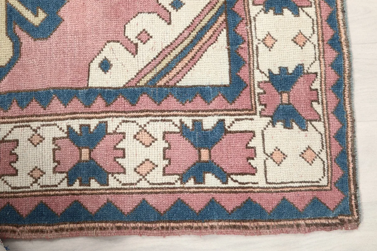 Detail of the rug's ivory and navy border with pink geometric patterns and outer navy sawtooth design.