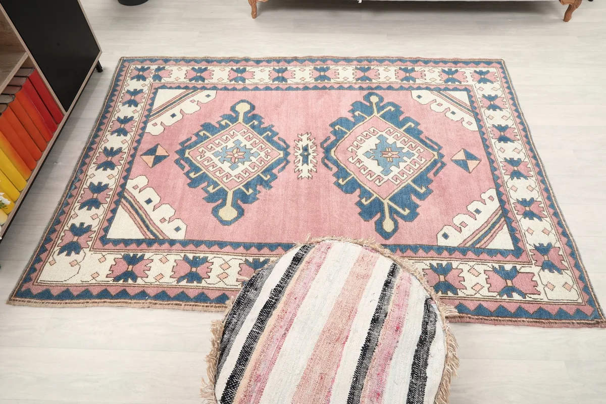 Full overhead view of the rose and navy geometric rug in a room, with a striped pouf in the foreground.