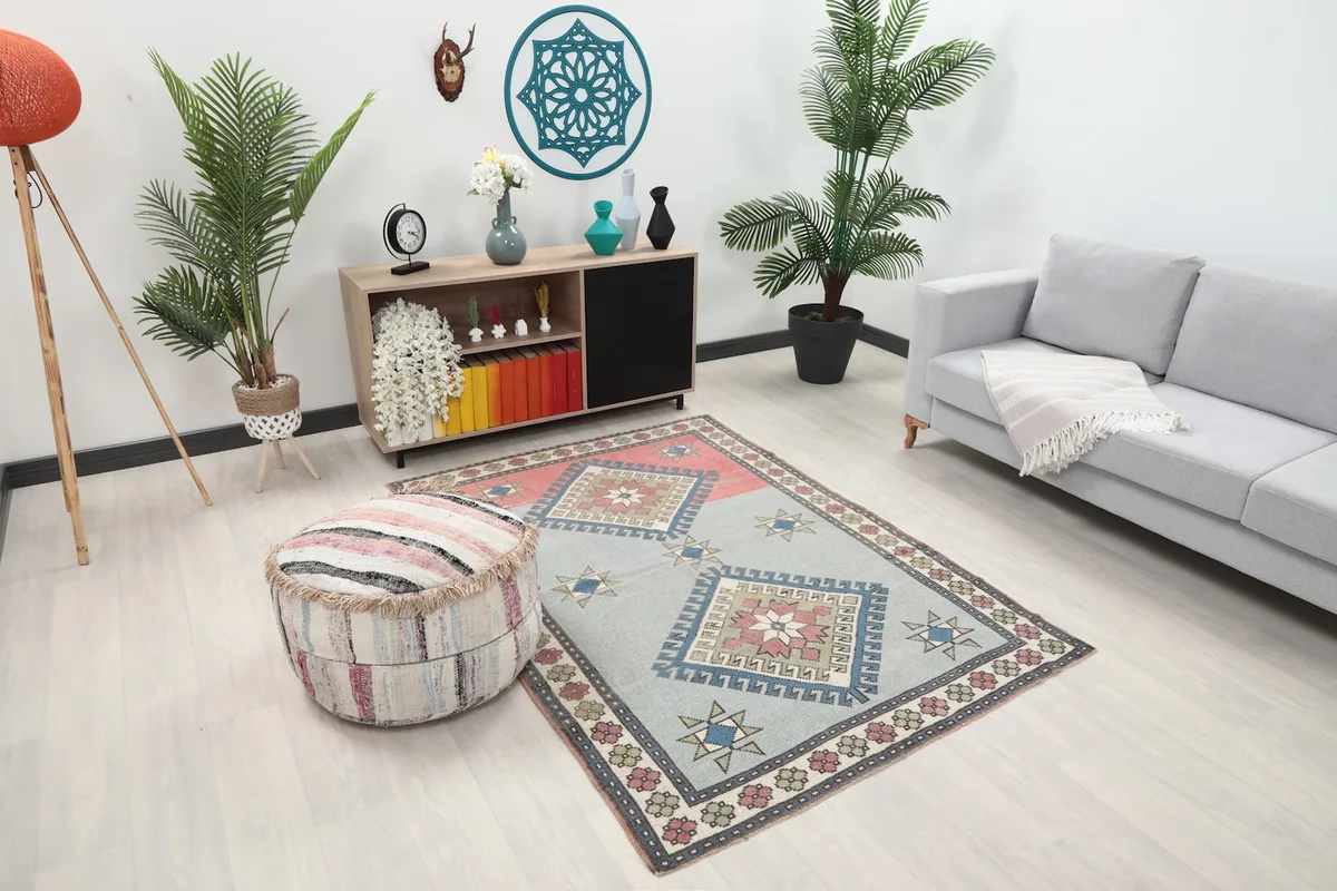 Angled view of the blue and rose rug in a living space with a striped ottoman