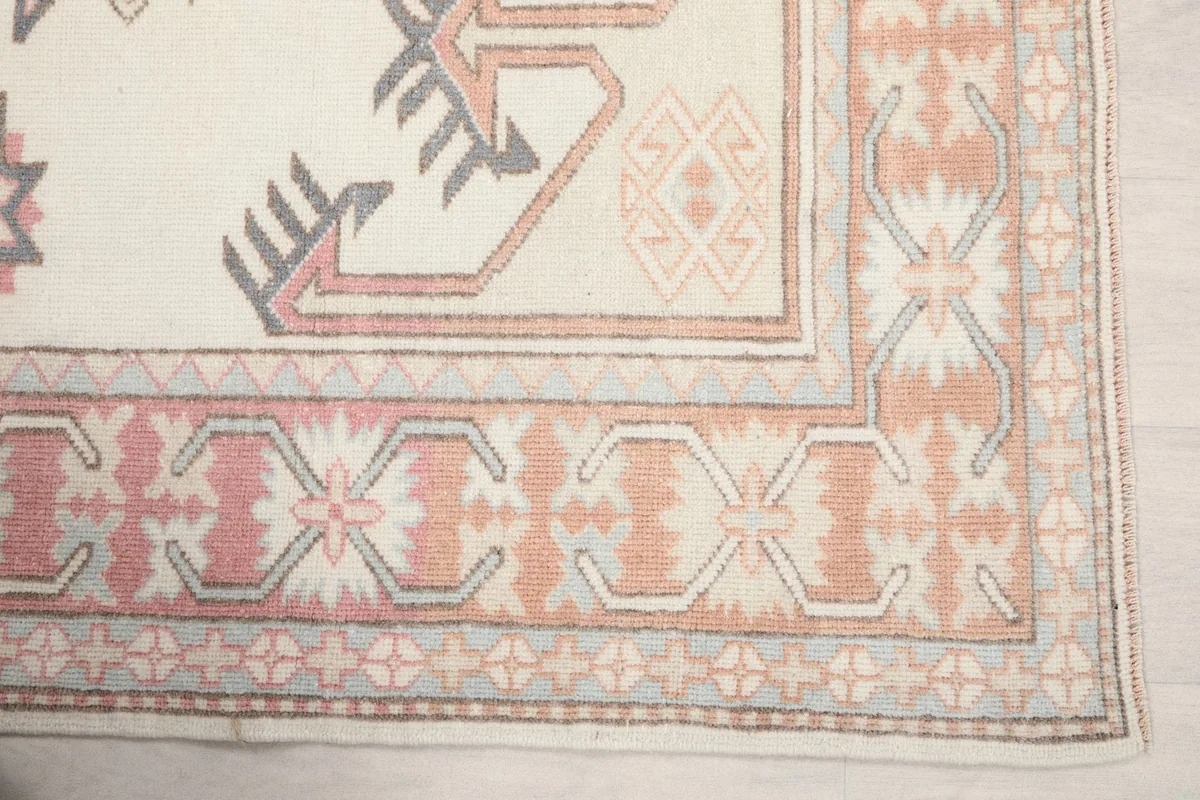 Detail of the pink and orange border design and corner motifs of the vintage wool rug