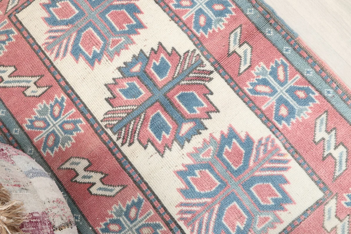 Angled view of the rug's central ivory panel and surrounding rose field with blue geometric patterns.