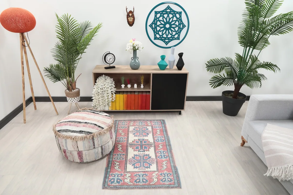 Rose and ivory geometric rug displayed in a living room setting next to a light gray sofa and wooden cabinet.