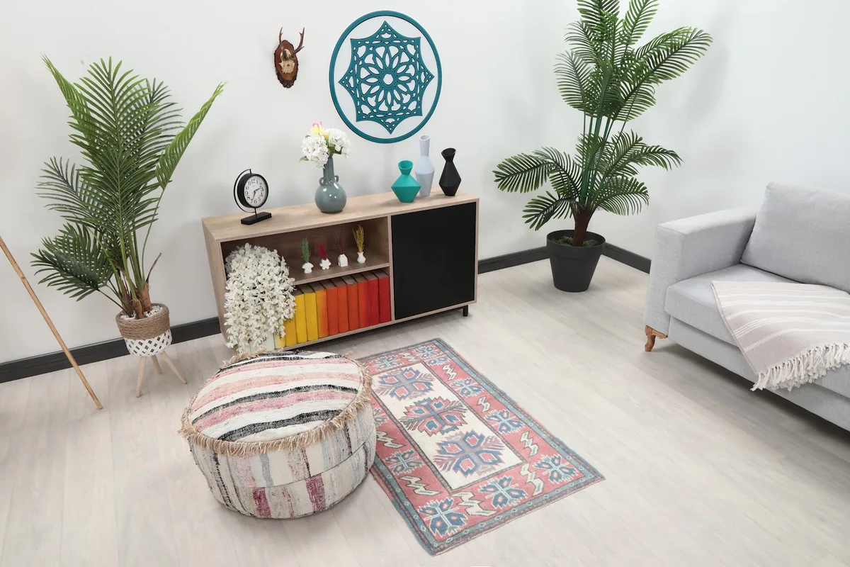 Vintage Anatolian rug with rose and blue motifs placed in a modern room with green plants.