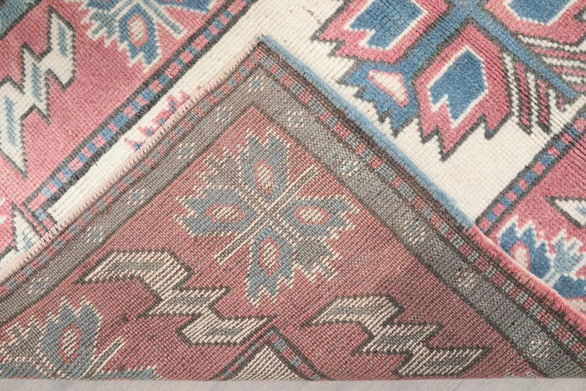 Folded corner of the rug revealing the cotton foundation and the reverse side of the hand-knotted wool pile.