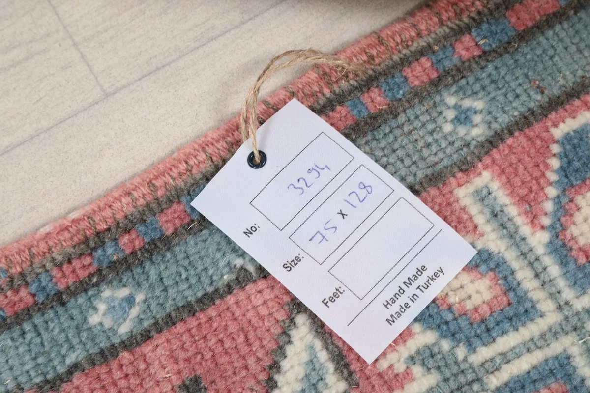 Product tag showing the rug's size (75 x 128 cm) and origin (Hand Made in Turkey), resting on the rug.