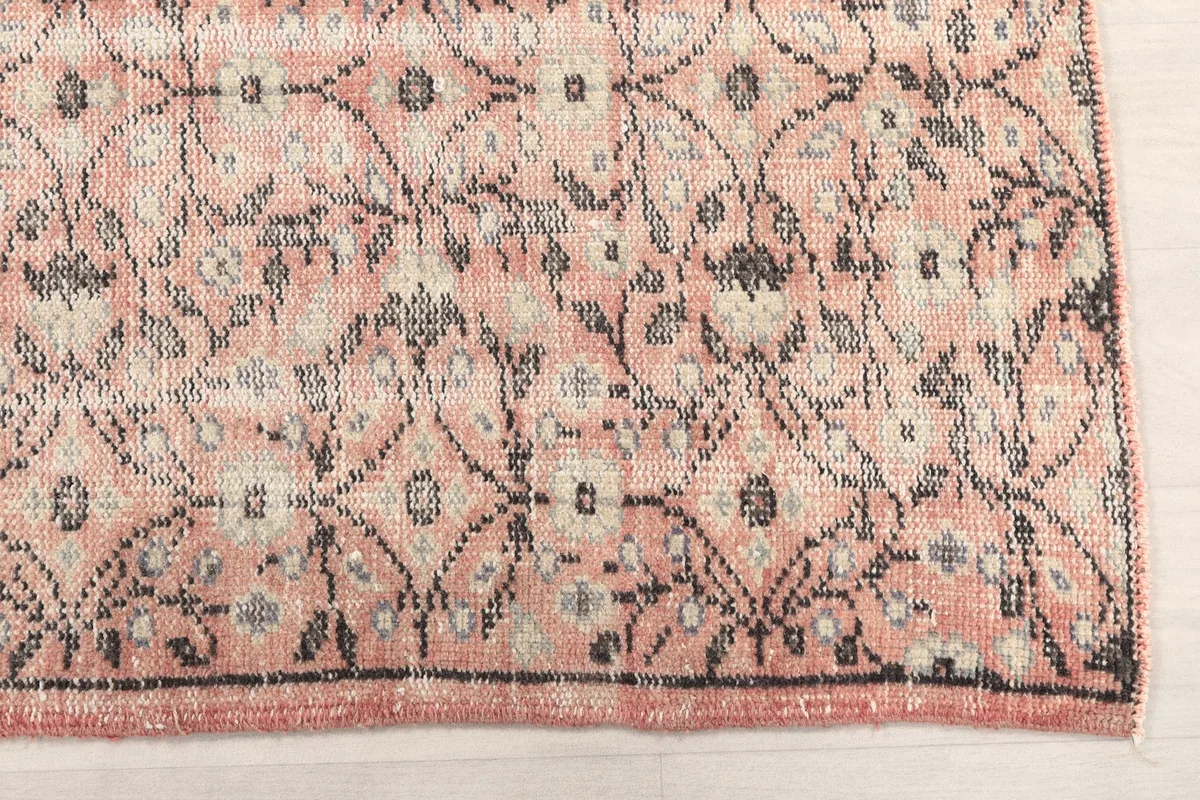 Close-up detail of the rug's pattern, highlighting the gray and beige floral motifs against the rose background.