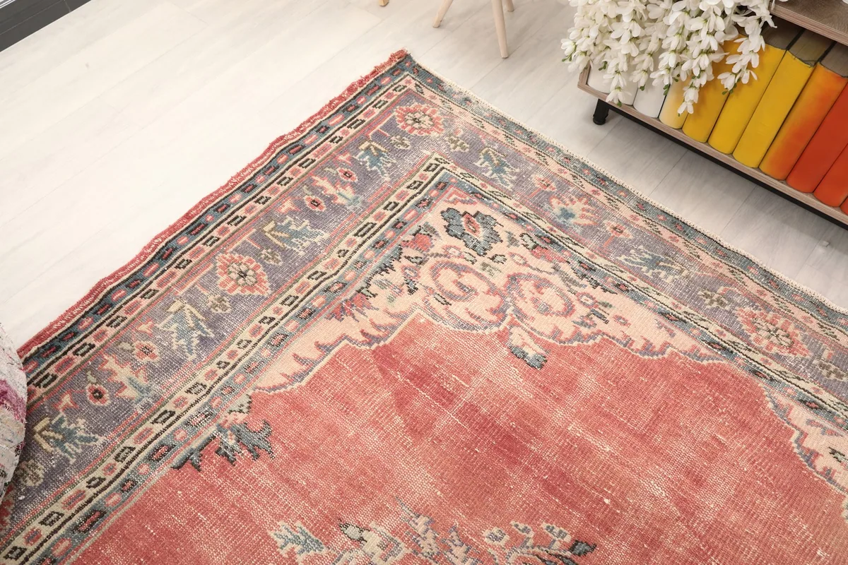 Corner view of the rug, showing the blend of rose field and gray border in a room setting.