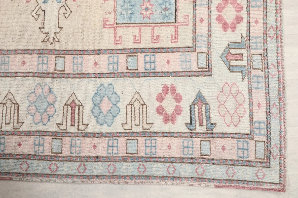 Detail of the rug's border with light blue, pink, and ivory geometric tribal motifs