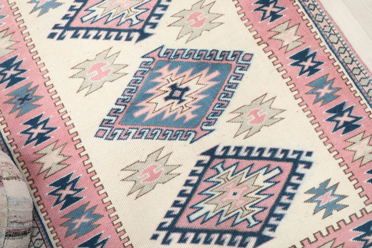 Detailed view of the central ivory field and geometric diamond motifs in pink and blue