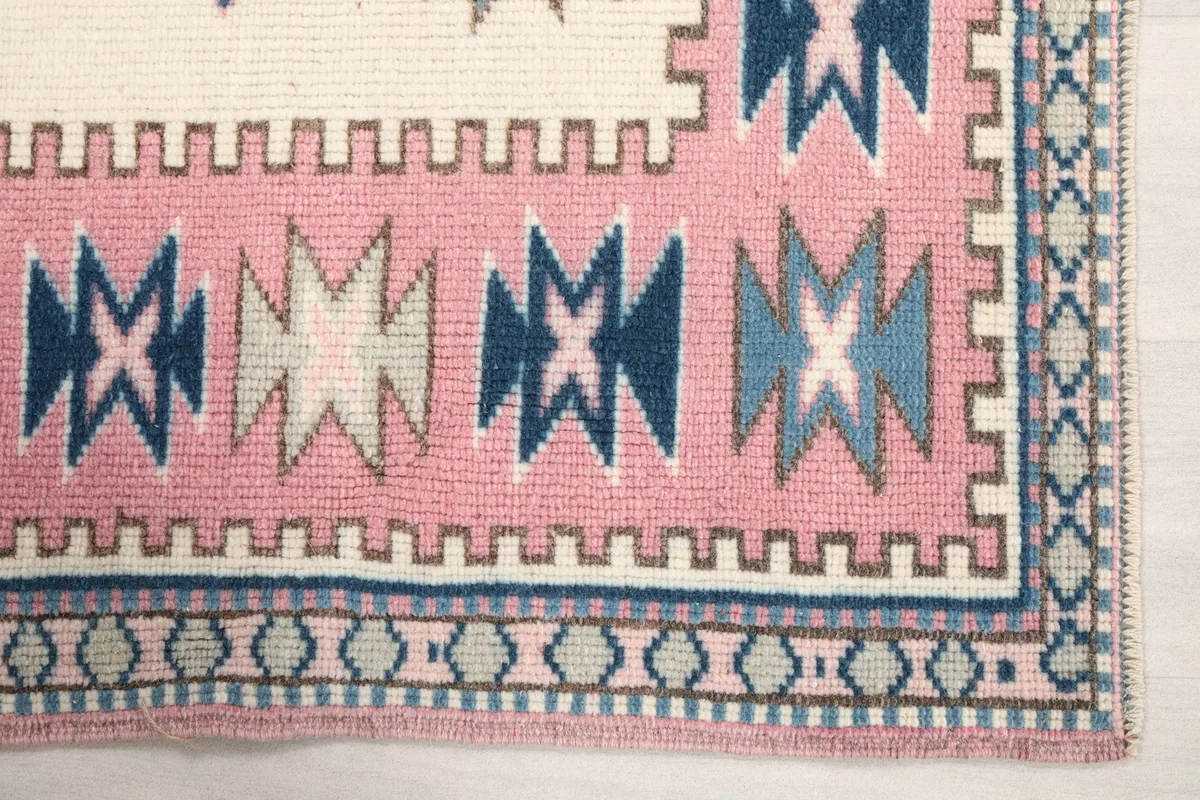 Close-up detail of the pink border with blue and gray tribal motifs on the rug