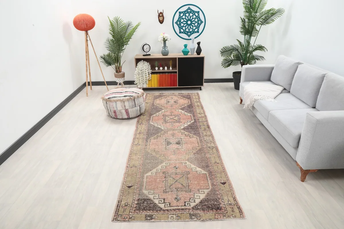 Rose and brown geometric runner displayed in a modern living room setting with a sofa and plants