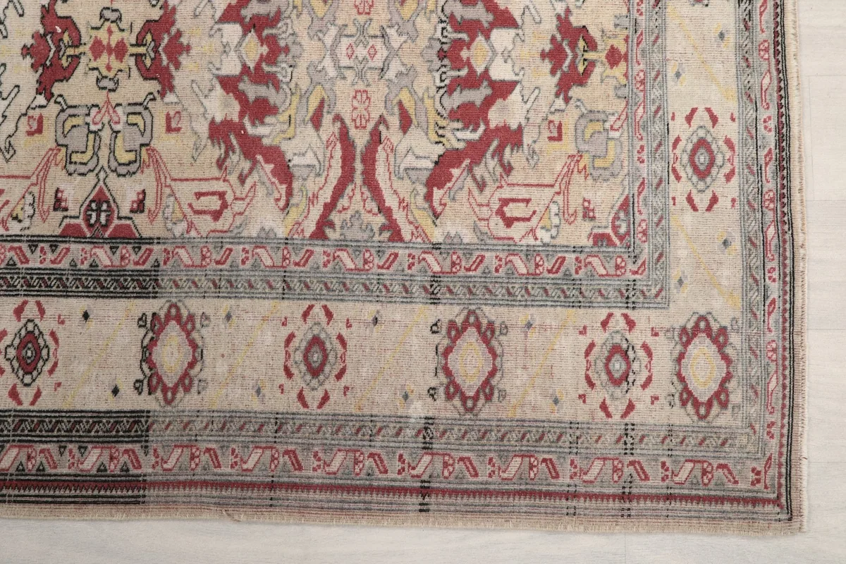 Detail of the rug's corner and border, showing gray and red accents on the ivory background