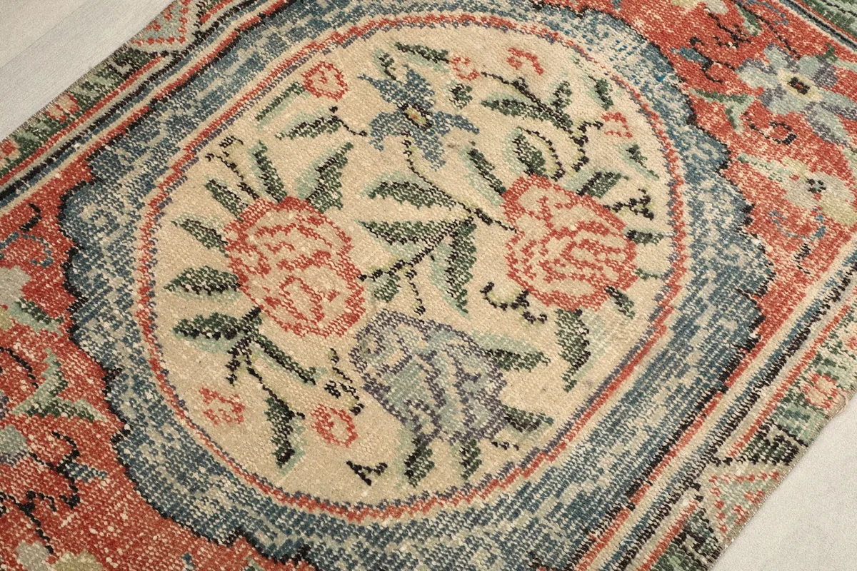 Detail view of the central ivory floral medallion with rose and blue elements on the vintage rug
