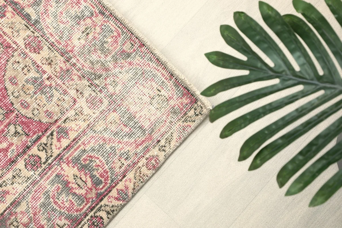 Angled view of the rug's border and a corner, with a green plant leaf in the foreground