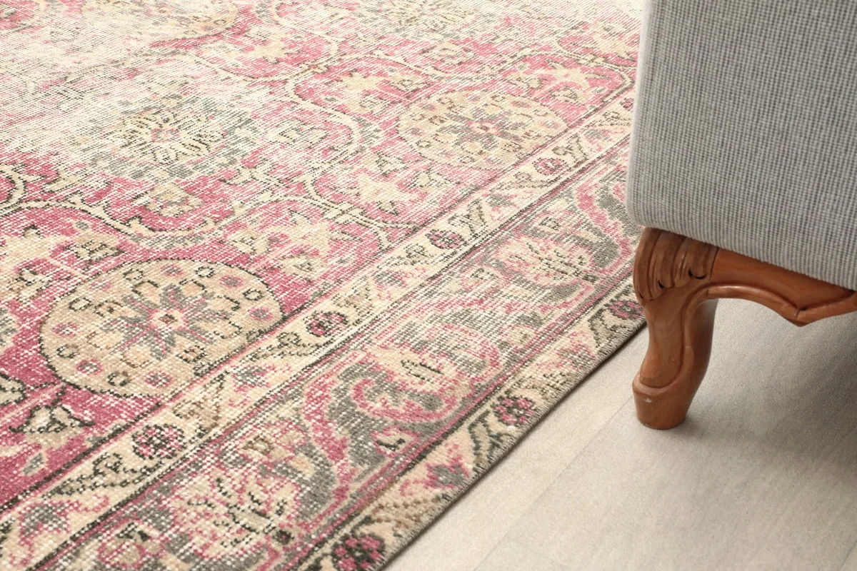 Close-up of the low pile texture and faded rose and beige colors near a sofa leg