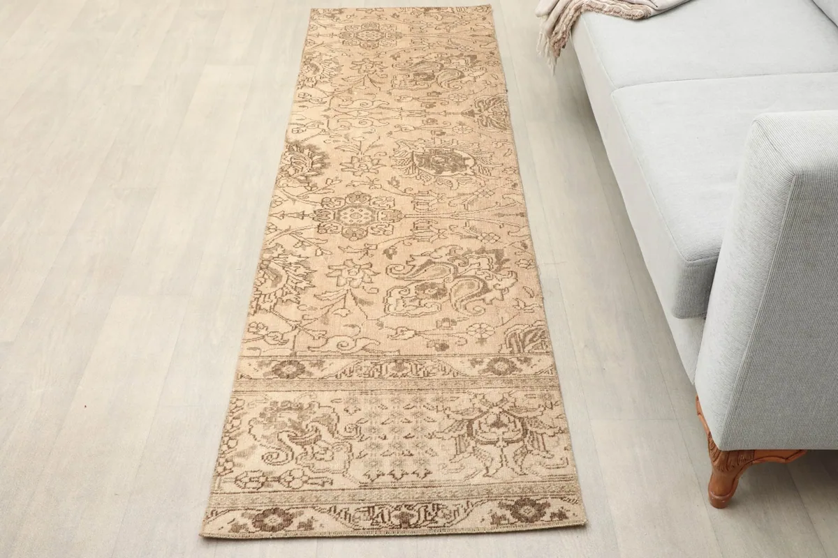 Vintage Anatolian runner placed in a living room next to a light gray sofa, viewed from an angle.